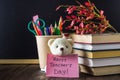 Concept of Teacher's Day. Objects on a chalkboard background. Books, green apple, bear with a sign: Happy Teacher's Day, pencils