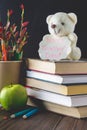 Concept of Teacher's Day. Objects on a chalkboard background. Books, green apple, bear with a sign: Happy Teacher's Day, pencils