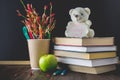 Concept of Teacher's Day. Objects on a chalkboard background. Books, green apple, bear with a sign: Happy Teacher's Day, pencils