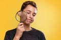 The concept of teenage acne. A teenage boy with a disgruntled face, holding a magnifying glass near the cheek with pimples. Yellow