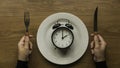 Concept of time and eating with a hand holding fork and knife and a vintage alarm clock on a white plate Royalty Free Stock Photo