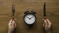 Concept of time and eating with a hand holding fork and knife and a vintage alarm clock on a wooden table Royalty Free Stock Photo