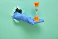 The concept of time and quarantine measures for coronavirus. A hand in a blue protective glove holds an hourglass