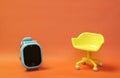 Concept of vacant chair. Yellow stool with blue kid smart watch on orange clean background. Photo in minimal style