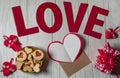 A blank sheet of paper, an envelope, a gift box, homemade cookies, wooden letters and red hearts on a light wooden background.