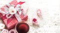 The concept of Valentine`s Day and Mother`s Day, a red gift box with a bow with roses and a cup of tea on a light wooden Royalty Free Stock Photo