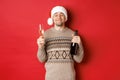 Concept of winter holidays, christmas and celebration. Image of pleased smiling man in santa hat and sweater, drinking