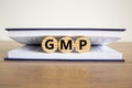 Concept word `GMP, good manufacturing practice` on wooden circles between pages of a book on a beautiful wooden table. White