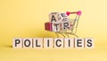 Concept word POLICIES on wooden cubes on yellow background with shopping cart and cubes
