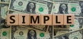 Concept word `simple` on wooden cubes on a beautiful background from dollar bills. Business concept