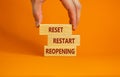 Concept words `reset, restart, reopening` on wooden blocks on a beautiful orange background. Male hand. Business concept. Copy