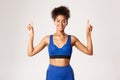 Concept of workout and fitness. Smiling fit and healthy african-american female athelte, wearing blue uniform, pointing