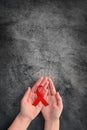 Concept World AIDS Day. Hands of woman holding red ribbon on black background. Blood transfusion and donation. Hemophilia day. Royalty Free Stock Photo