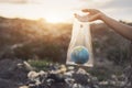 The concept of world environment day. The woman hand holds the earth in a plastic bag on garbage pile in trash dump or landfill ba