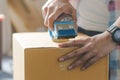 Concept young couple moving house. Close-up hand of woman use tape sealing cardboard box Royalty Free Stock Photo