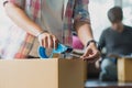 Concept young couple moving house. Close-up hand of woman use tape sealing cardboard box Royalty Free Stock Photo