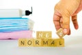 Conceptual adapting to new normal as lifestyle due to Covid-19. Wooden block letters and hand holding a cube over white. Face Royalty Free Stock Photo