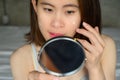 Portrait of young Asian woman holding mirror and applying acne cream/moisturizer on her face for treat her skin. Royalty Free Stock Photo