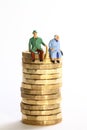 miniture figure retired couple sat on a stack of pound coins