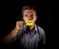 Conceptual dramatic portrait of young depressed man holding paper with happy smiley mouth draw on his lips looking miserable and f Royalty Free Stock Photo