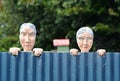 Conceptual funny nosy neighbours. Old man & woman looking over house fence Royalty Free Stock Photo