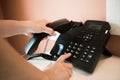 Closeup of female hand holding telephone receiver while dialing a telephone number to make a call using a black landline phone. Royalty Free Stock Photo