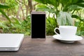 Conceptual green workspace,laptop with blank screen on table, coffee cup and green garden background, business technology conce