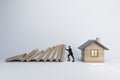 A conceptual image of a man preventing a falling row of dominoes from crashing into a small house, symbolizing protection and Royalty Free Stock Photo