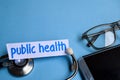 Public health inscription with the view of stethoscope, eyeglasses and smartphone on the blue background