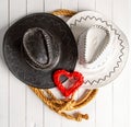 Conceptual image of rural wedding of cowboys. White bride hat and dark groom hat and red heart symbol of love