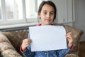 Conceptual image of a sad dejected little girl, holds a blank sheet of paper on gray background. Royalty Free Stock Photo