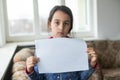 Conceptual image of a sad dejected little girl, holds a blank sheet of paper on gray background. Royalty Free Stock Photo