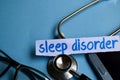 Sleep disorder inscription with the view of stethoscope, eyeglasses and smartphone on the blue background.