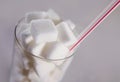 Conceptual macro still life image of refreshment glass full of sugar cubes and straw on white background in glucose addic