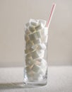 Conceptual macro still life image of refreshment glass full of sugar cubes and straw isolated on white background in glucose addic