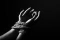 Conceptual monochrome image of woman hands tied with a coarse rope