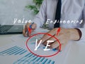 Conceptual photo about VE Value Engineering with written abbreviation. Business Man Checking Documents on background