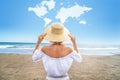 Conceptual photo of a women with straw hat enjoying sunny time at the beach. Back view. World map shaped clouds in the blue sky.