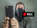 Conceptual portrait of young rioter filming street chaos . ultra and radical man masked recording riot video on mobile phone Royalty Free Stock Photo