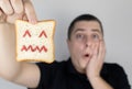 Conceptually about gluten intolerance. The man holds in his hand a piece of bread on which an angry expression is painted. Celiac Royalty Free Stock Photo