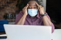 Concerned African-American man wearing protective medical mask staring at the laptop Royalty Free Stock Photo