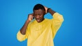 A concerned African man in a yellow hoodie grips his smartphone, frowning and touching his head Royalty Free Stock Photo