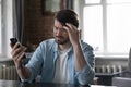 Concerned annoyed man staring at cellphone screen with upset face