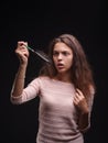 Girl struggling with tangled hair on the black background. Close-up woman looking at a comb with hair. Balding concept. Royalty Free Stock Photo
