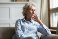 Concerned elderly woman lost in sad thoughts sitting on couch Royalty Free Stock Photo