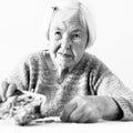 Concerned elderly woman sitting at the table counting money in her wallet. Black and white photo.