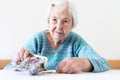 Concerned elderly woman sitting at the table counting money in her wallet.