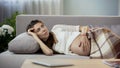 Concerned future mom lying on sofa, gently rubbing belly, thinking of future