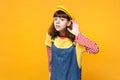 Concerned girl teenager in french beret and denim sundress eavesdrop with hearing gesture isolated on yellow wall