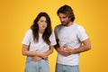 Concerned man and woman with pained expressions holding their stomachs